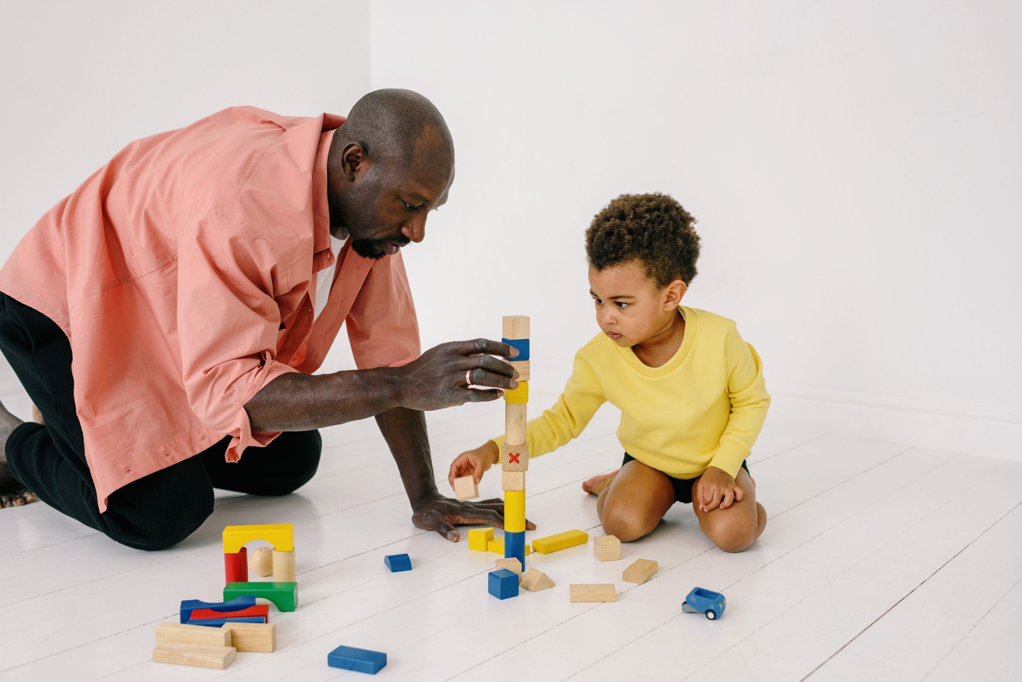 An adult and a young child building a tall tower of wooden blocks together on the floor