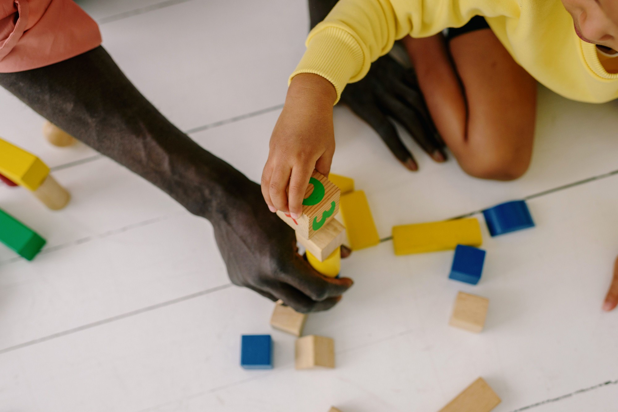 A child's hand and an adult's hand stacking wooden building blocks together