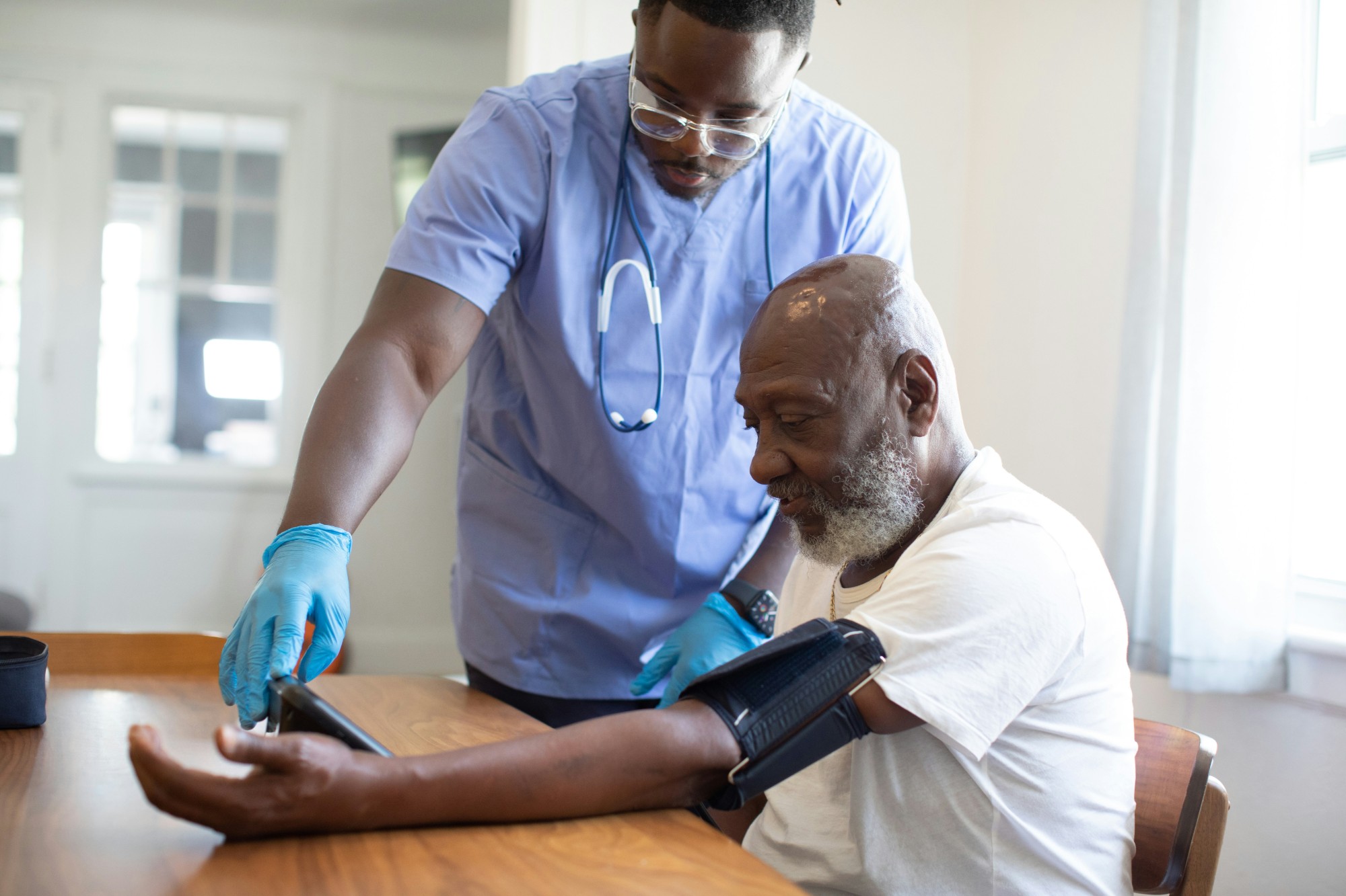 A therapist checking an older man's blood pressure at his dining table at home